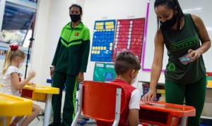 Volta às aulas durante a pandemia em uma escola particular do Distrito Federal. Crianças com máscaras estão sentadas em cadeiras próximas de professoes em uma sala de aula" Fonte: Andressa Anholete - Getty Images / ⓒ Direitos Reservados.